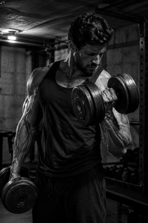 muscular man lifting dumbbells in a basement gym
